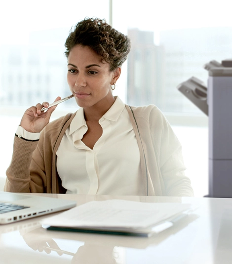 Woman at desk looking at computer with printer in the background